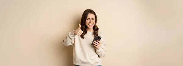 Fiatal Mosolyog Mutatja Hüvelykujját Miközben Használja Mobiltelefon Smartphone App Álló — Stock Fotó