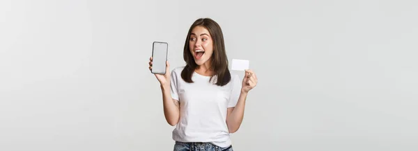 Podekscytowany Zaskoczony Cute Girl Pokazując Karty Kredytowe Telefon Komórkowy Aplikacji — Zdjęcie stockowe