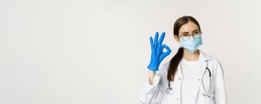 Coronavirus 'un yüz maskesi takan kadın doktorunun portresi. Onaylama, tavsiye, övgü ve güzel bir şekilde beyaz arka planda dikilme işaretini gösteriyor..
