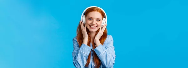 ウエストアップショット陽気ですかなりFoxy Caucasian女の子大規模なヘッドフォンで音楽を聞いて チェックアウトの友人のシングル ナイトウェアを着て 青の背景を立って喜んで — ストック写真