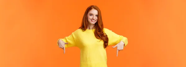 これを見て それをチェックしてください 黄色のセーターの陽気な豪華な赤毛の女の子は 笑顔と下を指して 製品をお勧めします 広告ショッピング休日の販売 オレンジの背景 — ストック写真