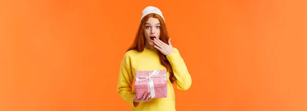 stock image Girl surprised didnt expact gift from you. Amused and startled cute redhead girlfriend open mouth, cover it with hand as receive cute pink box of present, look camera excited, orange background.