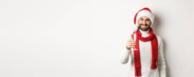 Noel partisi ve tatil konsepti. Sakallı yakışıklı genç adam, yeni yıl arifesinde kadeh kaldırıyor, elinde bir bardak şampanya ve gülümsüyor, beyaz arka plan.