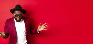 Kırmızı arka planda şarkı söyleyen, mikrofona şarkı söyleyen, parti kıyafeti giyen, kırmızı arka planda duran tutkulu siyah erkek şarkıcı..