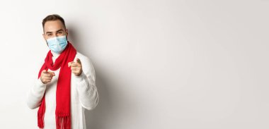 Covid-19, tecrit ve karantina konsepti. Yüzü maskeli mutlu adam seni işaret ediyor, tebrik ediyor ya da tebrik ediyor, beyaz bir geçmişi var..