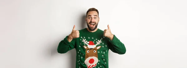 クリスマス 休日やお祝い 白い背景の上に立って 素晴らしい何かのように 親指を示す緑のセーターの興奮した髭の男 — ストック写真