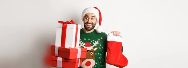 クリスマスと冬の休暇の概念 クリスマスの靴下とギフトボックスを持っている興奮した男は 新年を祝い 白い背景の上に立って — ストック写真