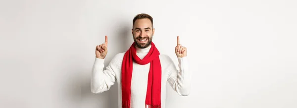 クリスマスショッピングと冬の休暇のコンセプト 髭を生やした笑顔の男がロゴを見せ 指を上げて幸せそうに見え セーターを着た赤いスカーフに立って 白い背景 — ストック写真