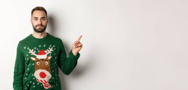 Kış tatili ve Noel. Yeşil kazaklı yakışıklı adam, gösteriş yapıyor, tanıtım yapıyor, beyaz arka planda duruyor..