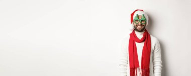 Noel, yeni yıl ve kutlama konsepti. Mutlu adam gülüyor, Noel Baba şapkası ve parti gözlüğü takıyor, beyaz arka planda duruyor..