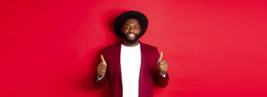 Noel alışverişi ve insanların konsepti. Yakışıklı siyah adam tatmin olmuş gülümsüyor, onaylıyor ve onaylıyor, kırmızı arka planda duruyor..