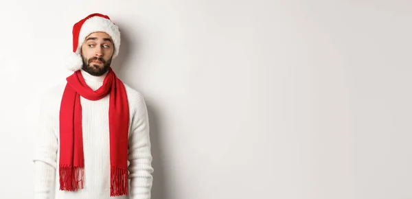冬休みと新年会のコンセプト 白い背景の上に立って クリスマスを祝う サンタの帽子に立って 左のロゴのバナーを見て好奇心旺盛な男 — ストック写真