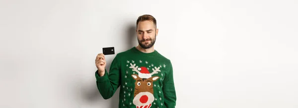 クリスマス休暇とショッピングのコンセプト 白い背景の上に立って考えている男はクレジットカードを見ている — ストック写真
