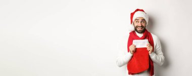 Kış tatili ve alışveriş konsepti. Heyecanlı yakışıklı adam yeni yılı planlıyor, elinde hediyeler için Noel çorabı tutuyor ve düşünüyor, beyaz arka planda duruyor..