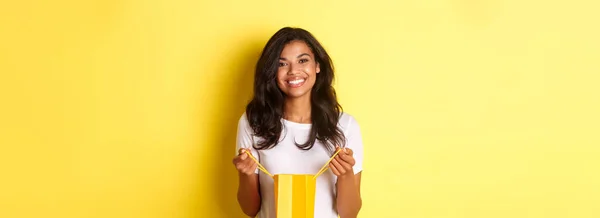 幸せなアフリカ系アメリカ人の少女の肖像画 休日の贈り物に感謝し 黄色の背景の上に立って ショッピング悪いと笑顔を開きます — ストック写真