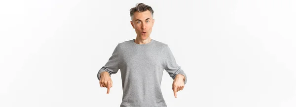 驚くべきハンサムな中年の男でグレーセーター製品についての質問を投げかけ 指を下に向け 驚いて 白い背景の上に立って — ストック写真