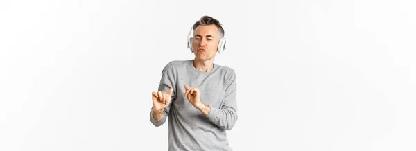 ハンサムな 現代的な中年の男の肖像 ヘッドフォンやダンスで音楽を聞いて 白い背景の上に立って — ストック写真