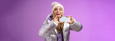 Gümüş ceketli, neşeli bir kadın. Kafası gülüyor. Elinde akıllı telefon kayıt videosu, ünlü cep telefonu kamerası, mor arka plan..