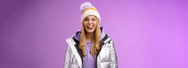ライフスタイル 生意気な屈託のない喜んで魅力的なブロンドの女の子楽しい楽しい感じ楽しい肯定的なショー舌笑顔広く身に着けている冬の銀輝くジャケットスタイリッシュな帽子素晴らしいスキー休暇を楽しんで — ストック写真