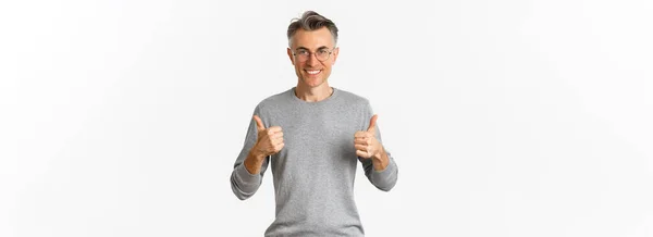 自信に満ち満ちた中年男性のイメージ 親指アップを示す グレーのセーターと眼鏡を身に着けています 白い背景の上に立って — ストック写真