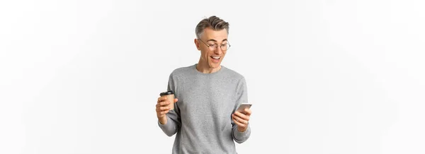 스웨터와 안경을 잘생긴 남자의 커피를 마시고 스마트폰 화면에서 보이는 — 스톡 사진
