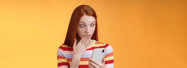 女人收到令人震惊的消息 屏住呼吸捂住嘴 盯着智能手机显示谁在跟踪男朋友的社交网络 站在令人惊讶的橙色背景下 — 图库照片