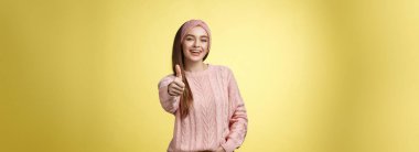 Jestler, duygular ve yaşam tarzı konsepti. Kendine güvenen 20 'li yaşlarda Avrupalı bir kadın sarı arka planda rahat bir süveter giyiyor başparmak hareketlerini gösteriyor, onaylıyor, kabul ediyor ve beğeniyor..