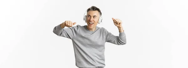 现代中年男人的画像 用耳机听音乐 站在白色背景之上 — 图库照片