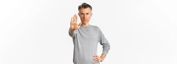 重大な中年男性のイメージは あなたを停止するには 悪い何かを禁止し 眉をひそめ 不満を見て 白い背景の上に立って片手を拡張します — ストック写真