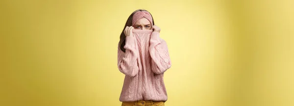 悲しい愚かな 悲観的なかわいい女の子隠れて顔でセーターの襟鼻の上に服を引っ張る不満 先住民と黄色の背景に失望立って見て — ストック写真