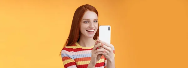 红头发姑娘开心地录着热闹的朋友们的动作举行智能手机看表演打趣的视频电话站着橙色背景满意地笑着 生活方式 — 图库照片