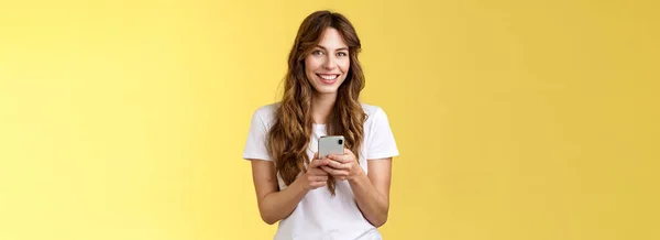 充满热情 善于社交的女孩给朋友发短信 社交媒体则拿着智能手机 开心地笑着站在黄色背景休闲装上 技术概念 — 图库照片