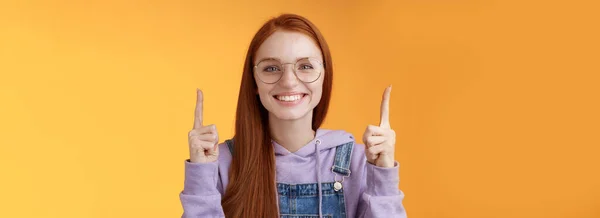生动活泼迷人的红头发女学生帮助指尖食指显示出令人敬畏的宣传效果提供笑容可亲的白牙表示广告推荐使用产品 — 图库照片