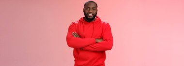 Çekici sakallı Afro-Amerikan genç adam kırmızı kapüşonlu çapraz kol göğsü takıyor arkadaşlara gülümsüyor yeni bir yer gösteriyor sırıtıyor kendi dairesini satın almaktan mutlu, gururlu pembe arka plan..