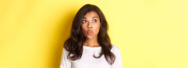 stock image Close-up of impressed african-american woman in white t-shirt, saying wow, looking at upper left corner advertisement, standing over yellow background.