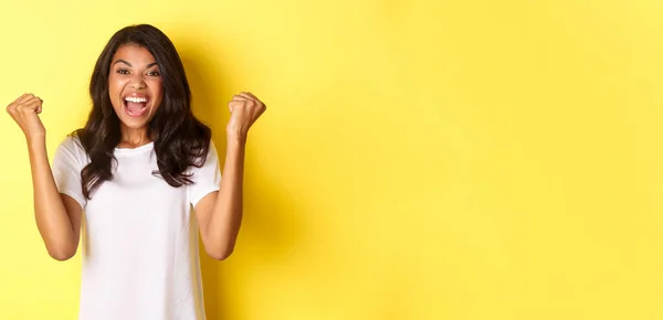 stock image Image of successful african-american girl, feeling lucky, making fist pump sign and saying yes, triumphing and shouting for joy, standing over yellow background.