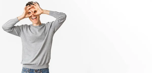 stock image Portrait of funny middle-aged guy making faces, showing hand glasses around eyes as if looking through binoculars, standing over white background.