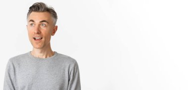 Yakışıklı, orta yaşlı, gri saçlı, ağzı açık, sol üst köşeden şaşkın, beyaz arka planda duran bir adam..