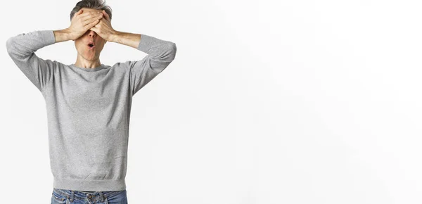 stock image Image of excited middle-aged guy in grey sweater, cover eyes with hands and looking amazed while waiting for surprise, playing hide-n-seek, standing over white background.