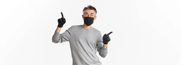 コロナウイルスの概念 ライフスタイルと隔離 白髪の中年男性のイメージ 黒い医療マスクを身に着けています 手袋や眼鏡 横に指を指して コピースペースを示します — ストック写真
