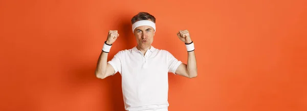 stock image Image of confident middle-aged male athlete, feeling good while working out, raising hands and triumphing, standing over orange background.