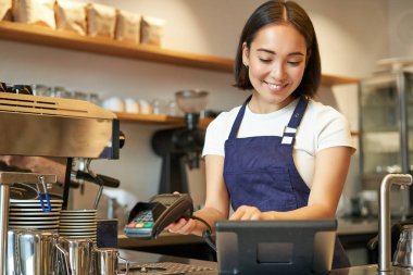 Gülümseyen Asyalı barista kız işlem sırası, POS terminaline girin, kahve dükkanında tezgahta çalışın..