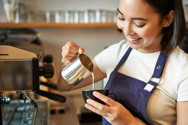 アジアのバリスタの女の子の笑顔 コーヒーを作る カプチーノに蒸しミルクを注ぐ カップでラテアートをする カフェで働く — ストック写真