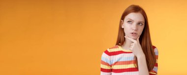 Zeki, yaratıcı, ciddi görünümlü, odaklanmış, düşünceli, düşünceli, seçimler yapan, çeneye dokunan, düşünceli, sol üst köşedeki, kafası karışmış, turuncu arka planı sorgulayan kızıl saçlı bir kadın..