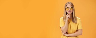Sorunlu ve endişeli genç bir kadın sorunlu bir sorunla karşı karşıya. Çene üzerinde el ele tutuşup dudaklarını büzüyor. Sağ üst köşeye dikkatlice bakıyor.