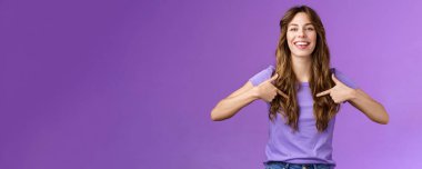 Gururlu, yakışıklı, kıvırcık Avrupalı bir kadın gururla sırıtıyor gururla sırıtıyor gururla sırıtıyor ve göğsünün ortasında geniş bir gülümseme beliriyor mor arka plan ile övünüyor. Yaşam biçimi.