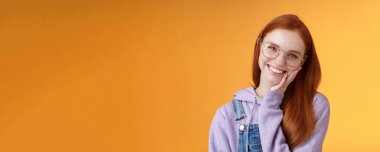 Gülümseyen mutlu kızıl saçlı kız kurtuluyor sivilceden zevk alıyor yumuşak, temiz tene dokunuyor neşeli bir şekilde gülüyor kendine güvenen bir güzellik hissediyor, turuncu arka planda duruyor iletişimin tadını çıkarıyor..