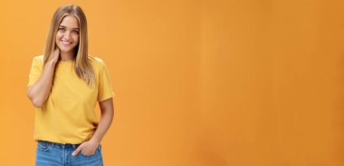 Çekingen ve ürkek kadın portresi, bronz tenli ve düz saçlarıyla boynu okşayan ve mutlu, tasasız bir ifadeyle gülümseyen turuncu arka planda el ele duran.