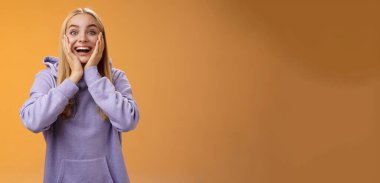 Şaşırtıcı derecede mutlu, şaşkın, sarışın kız arkadaş inanılmaz tatlı hediyeler alıyor. Çok tatlı, çok tatlı yanaklara dokunuyor, tatmin oluyor. Heyecanlı turuncu kapüşonlu arka planda dikiliyor..