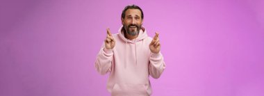 Umut dolu, iyimser, olgun, şık sakallı, modaya uygun kapüşonlu gri saçlı adam gergin bir şekilde mor arka planda dikilerek önemli sonuçlar beklemektedir..